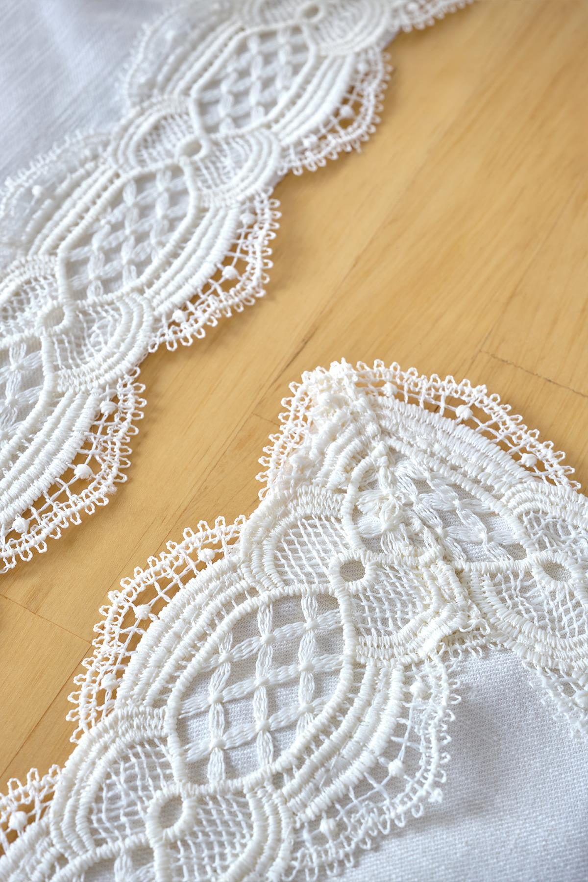 Cream-colored lace-embroidered table runner, detailed close-up shot on a wooden surface