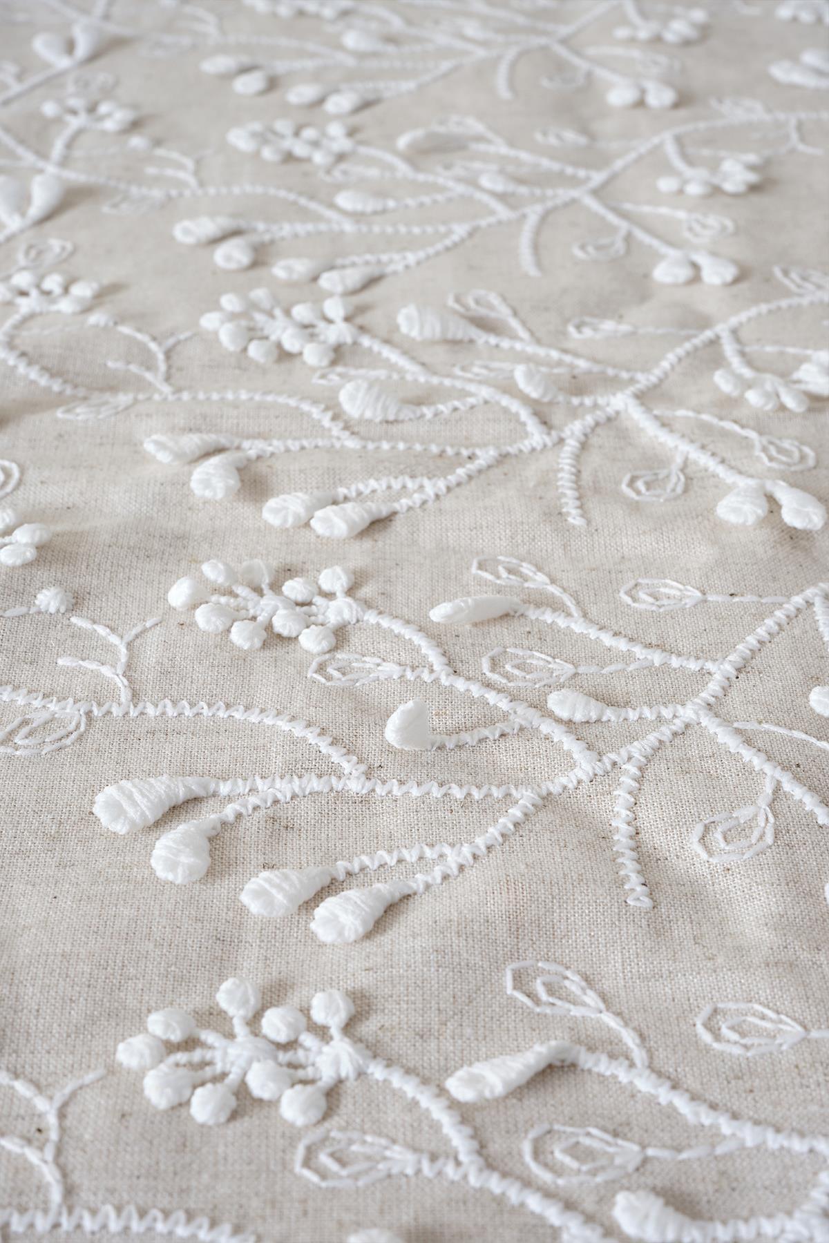 Close-up shot of fabric with white embossed floral embroidery on a beige background