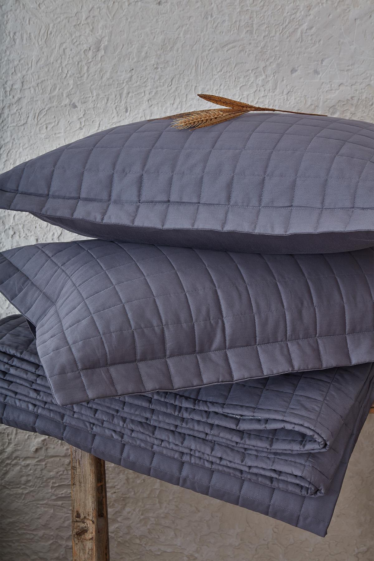 Quilted gray double bedspread and pillowcase, in front of natural decor