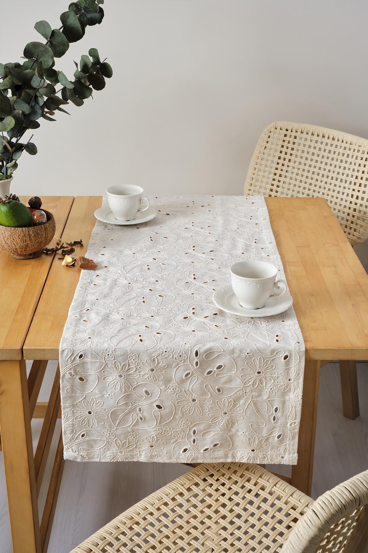 Cream-colored lace-embroidered table runner, decorative presentation with two cups on a wooden table