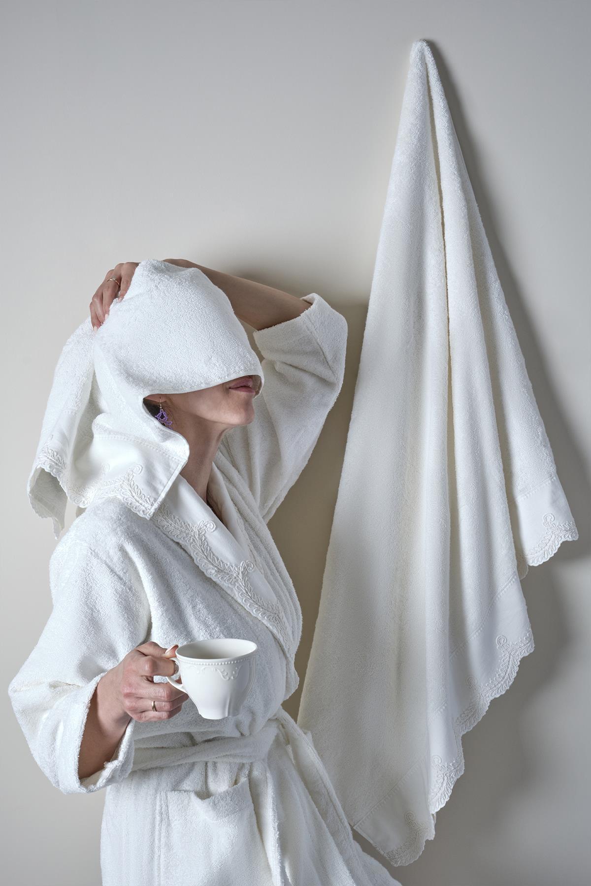 Woman in a white bamboo bathrobe holding a cup, with a towel hanging on the wall