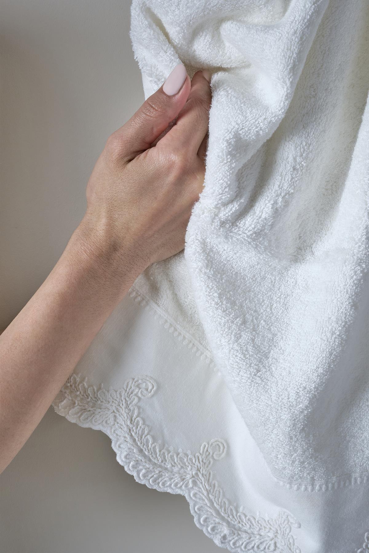 Hand-embroidered white hand towel with lace edge detail, held in hand