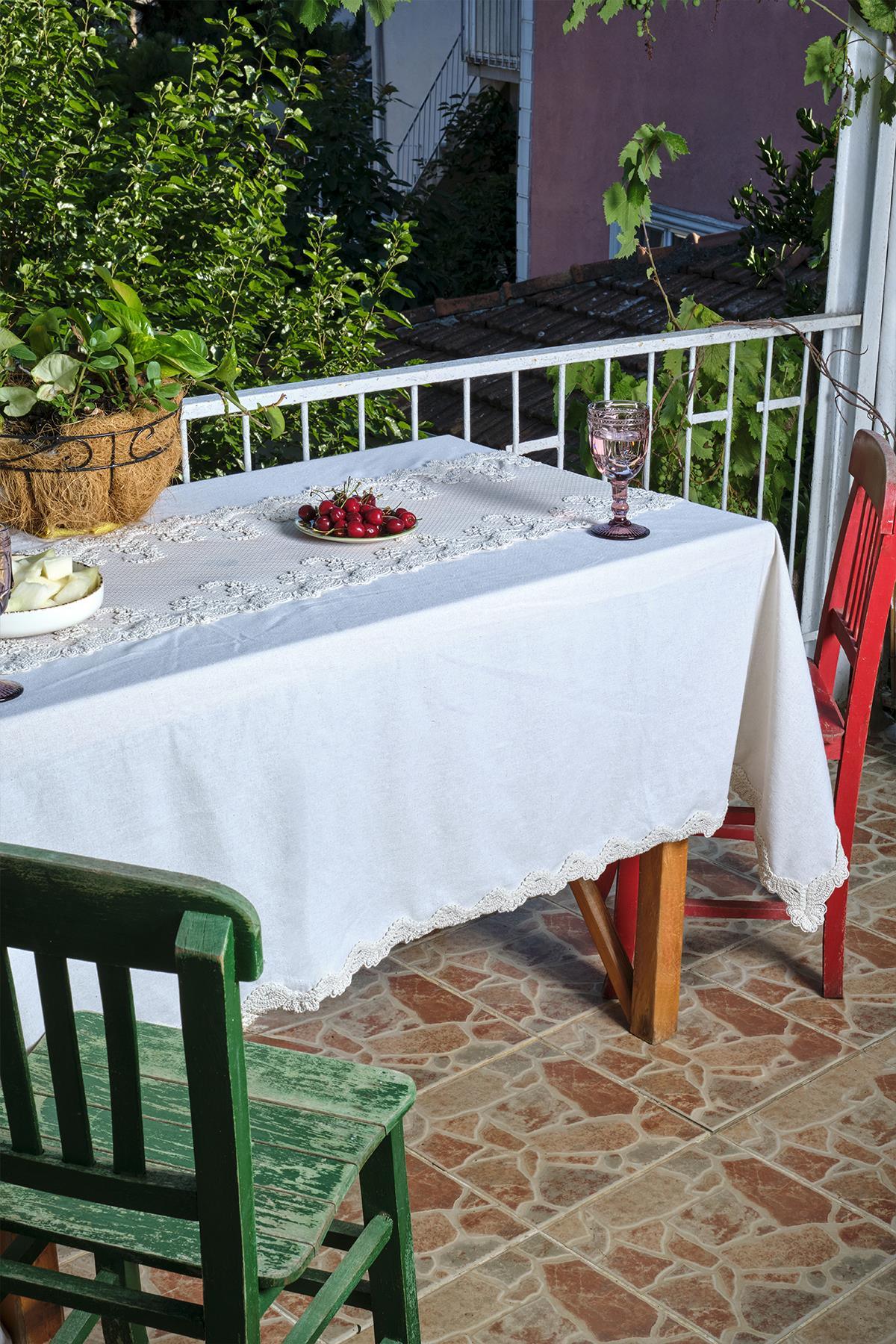 Balcony table covered with a white lace-detailed tablecloth, with red and green chairs next to it