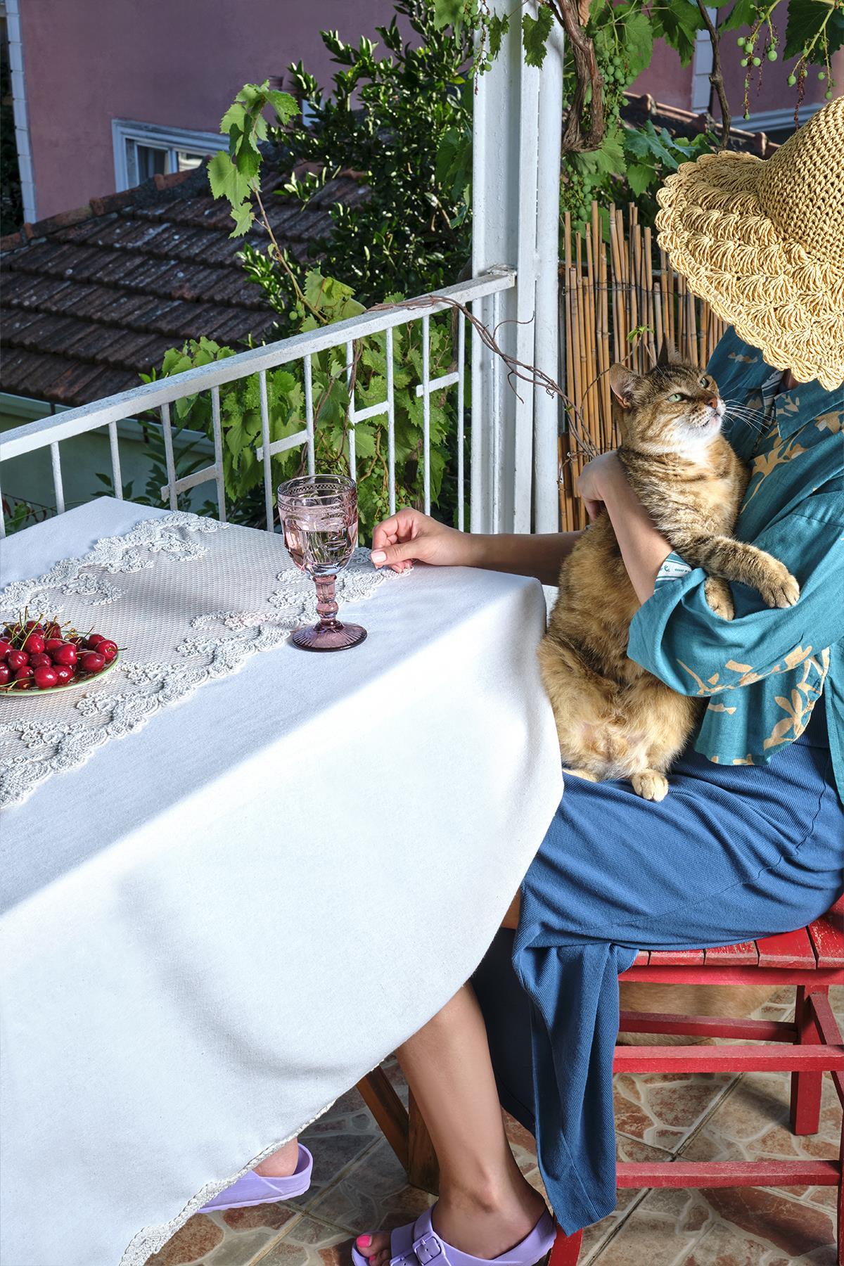 Lace-embroidered tablecloth on a balcony with cherry and pink glasses, and a cat nearby