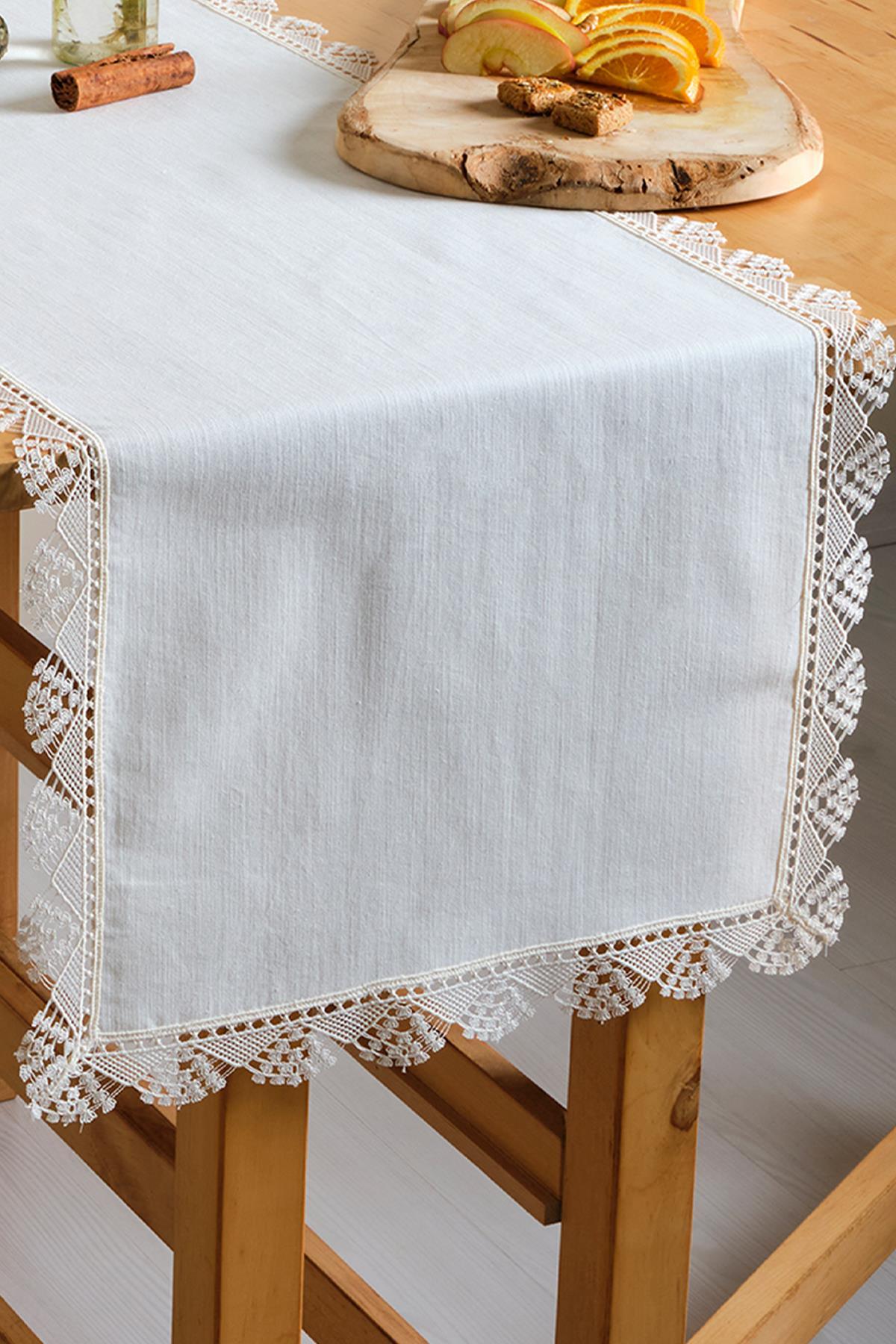 White lace table runner on a wooden table, decorated with fruit and cookies.