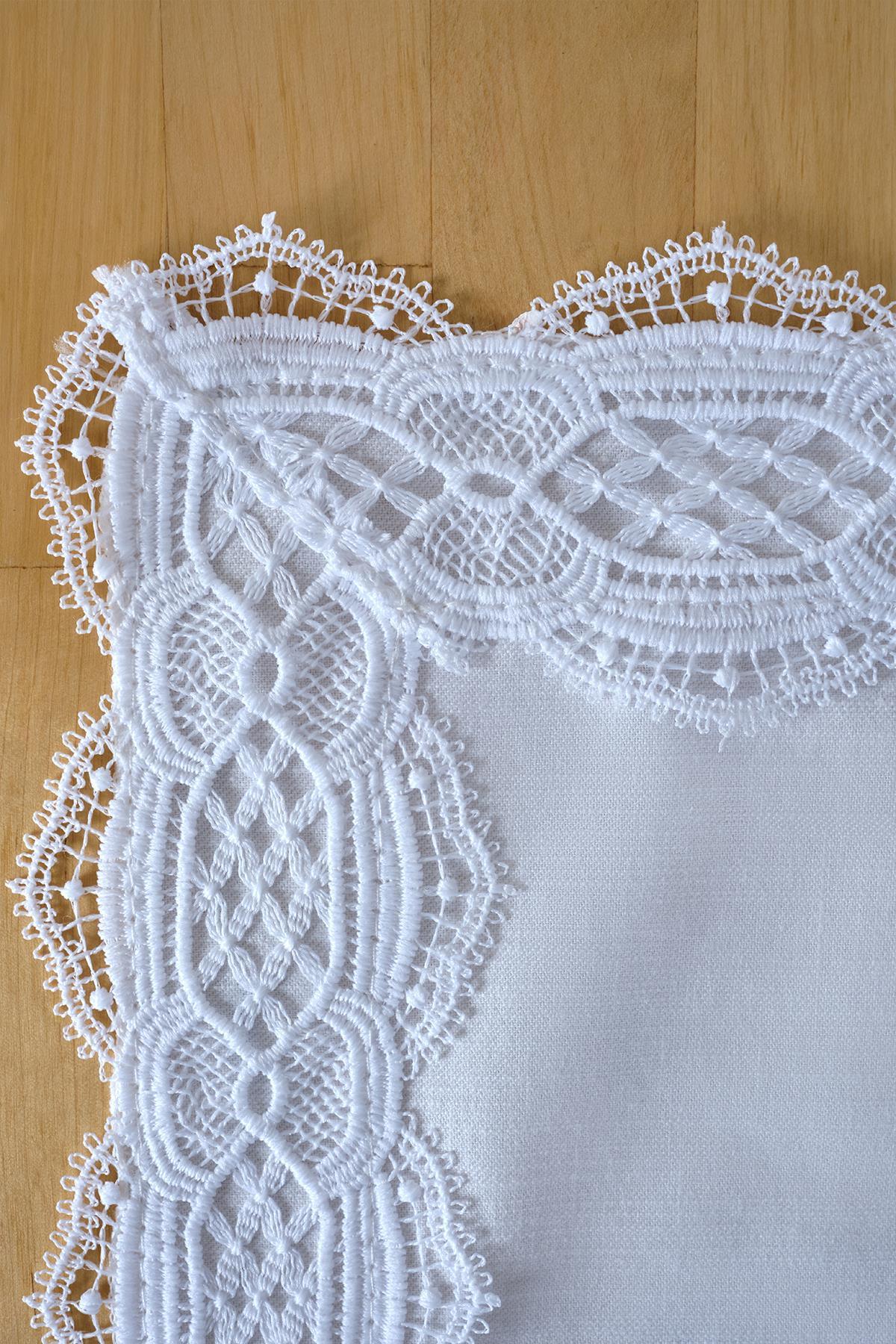 Corner of a white lace-embroidered table runner on a wooden floor