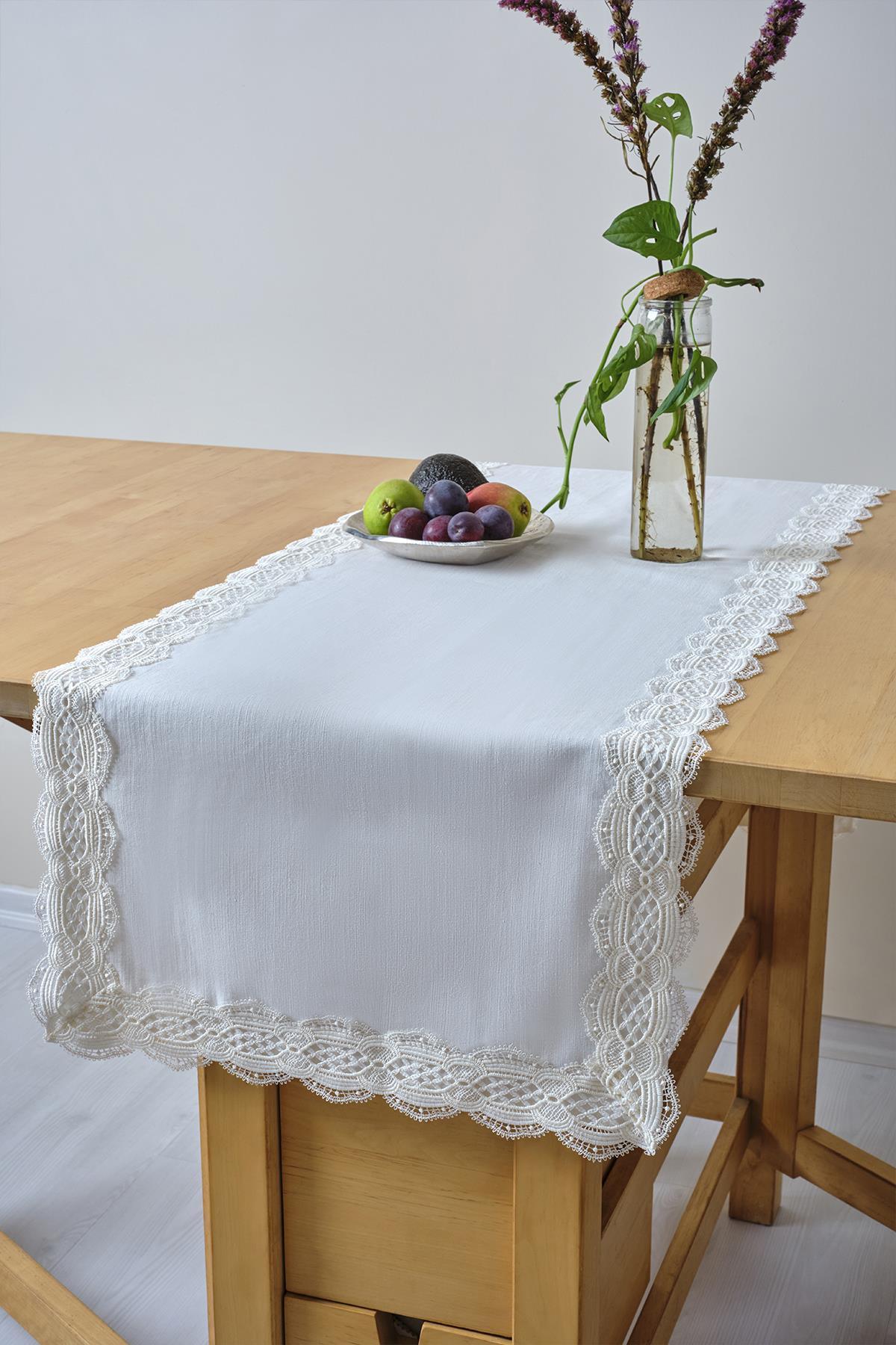 White table runner with lace detail, featuring a fruit bowl and glass vase on a wooden table