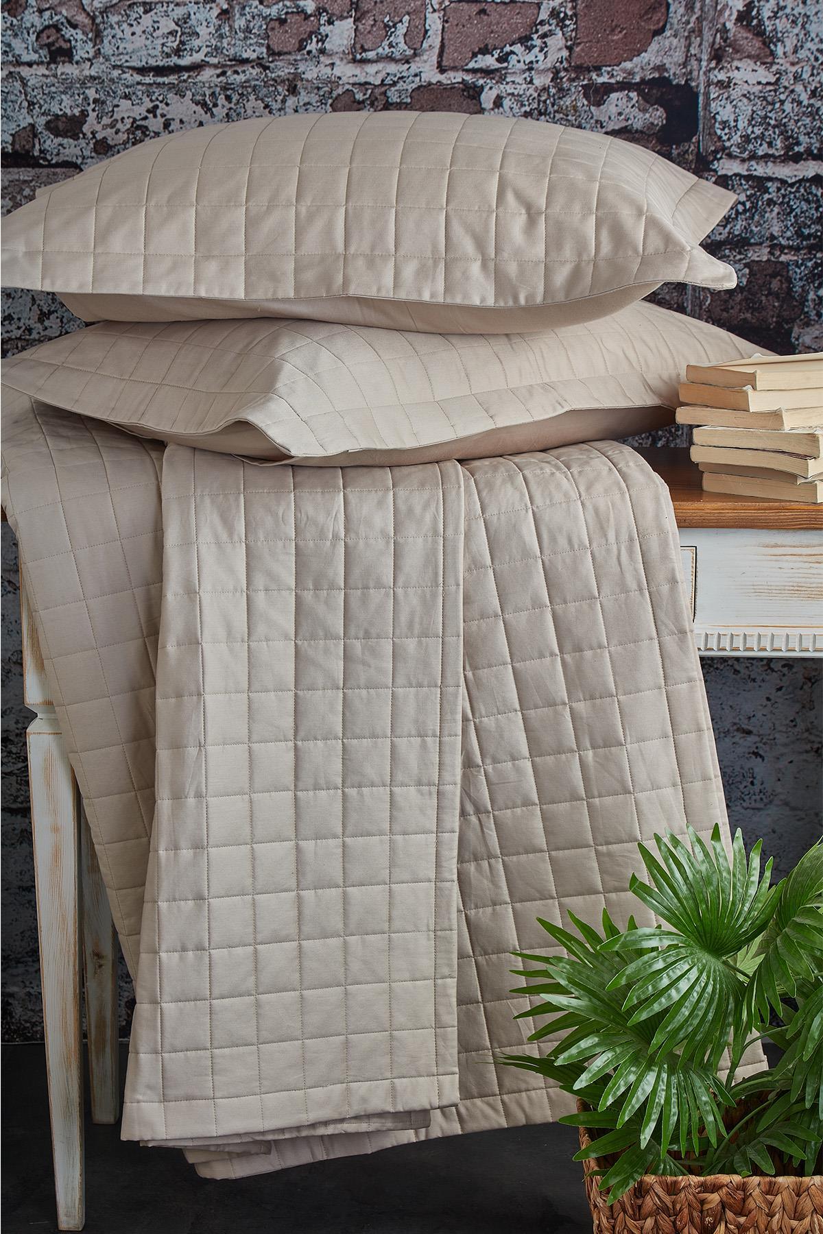 Quilted double bedspread, cream color, with two pillows, displayed on a table