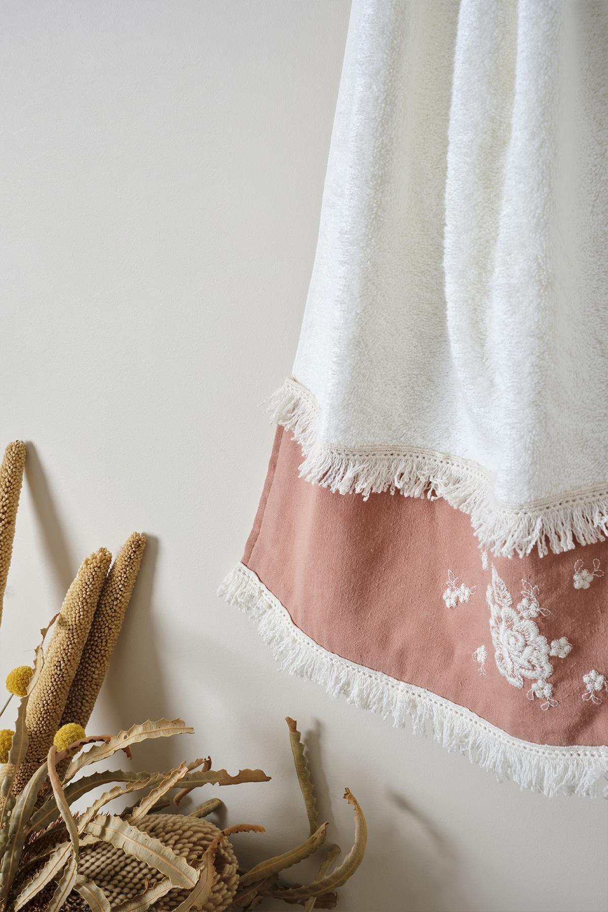 Small white towel with powder-colored embroidered edges and tassels, decorative bathroom towel