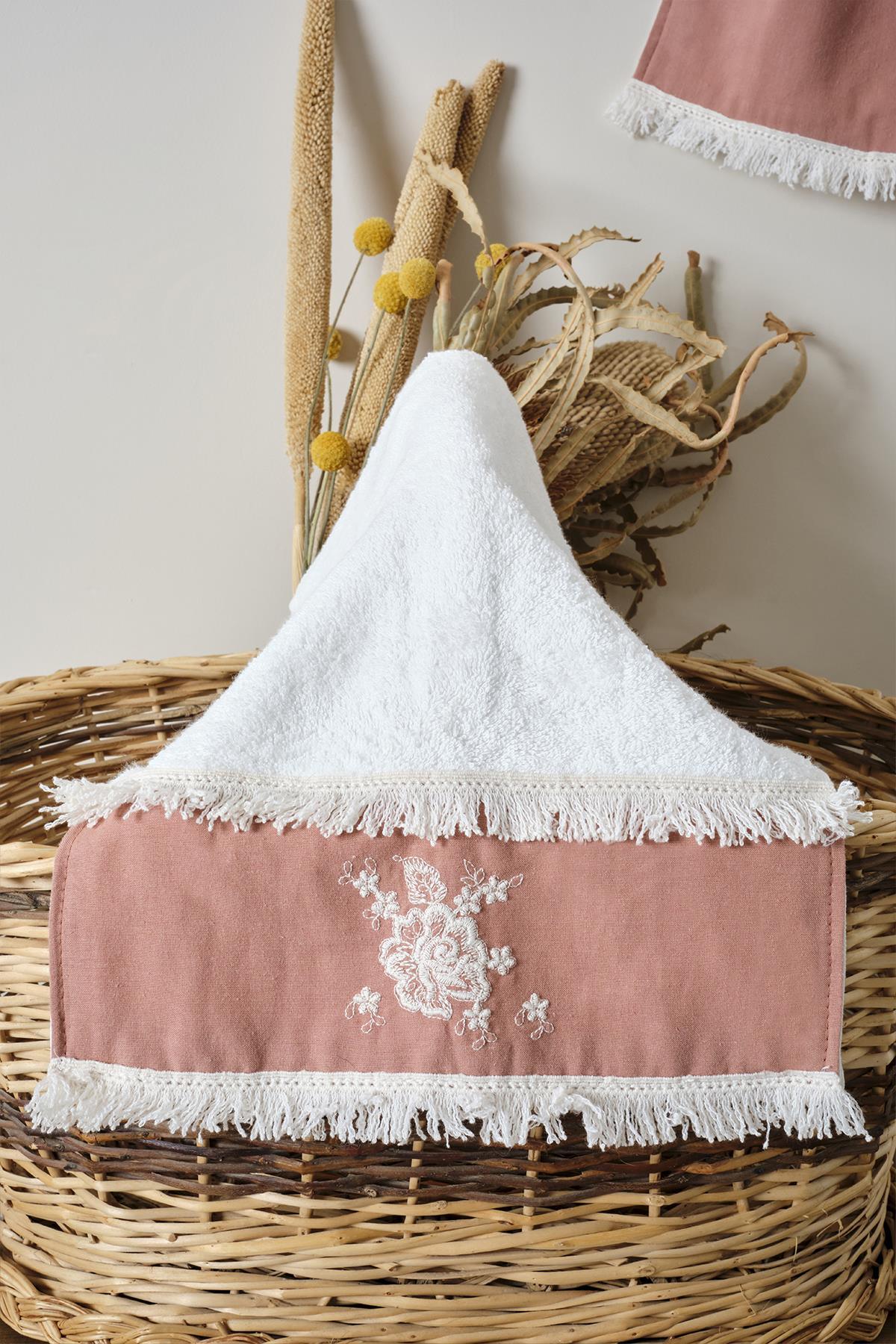 Powder-colored cotton towel with lace details and fringe, decorated with a wicker basket and dried flowers.