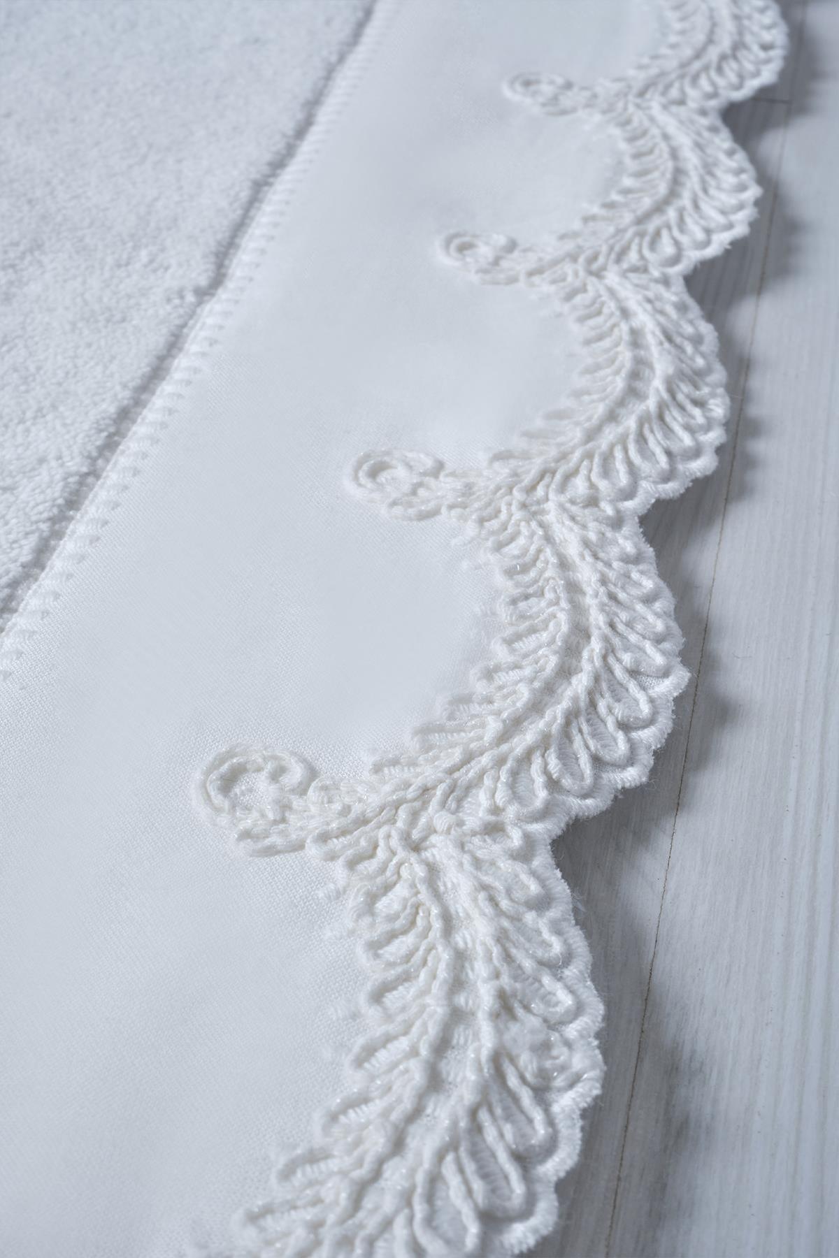 Close-up shot of a white cotton bath mat with lace embroidery details