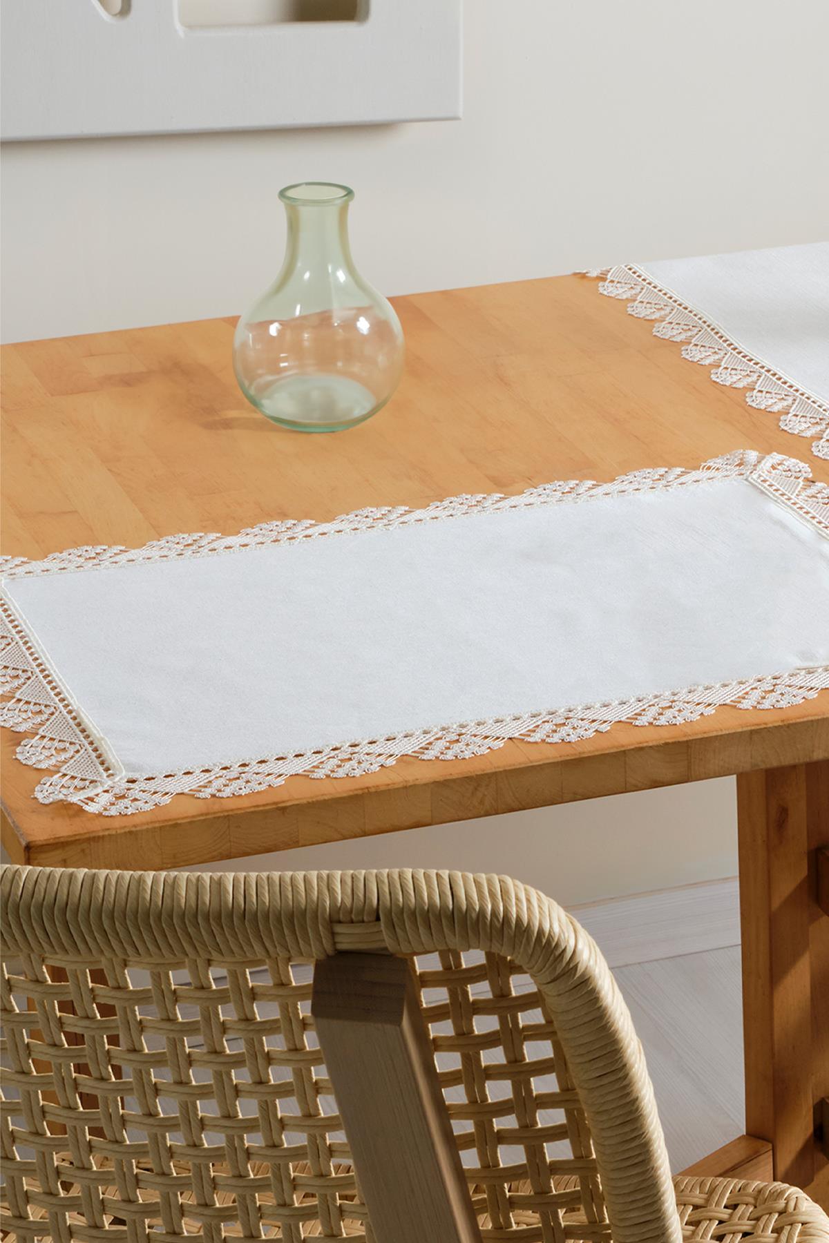 White placemat with lace trim on a wooden table, table decoration with a glass vase